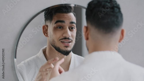 Funny arabian indian bearded man speaking to reflection looking in bathroom mirror. Smiling sexy millennial guy narcissist speaks to himself rehearses speech performance oratory affirmation in morning
