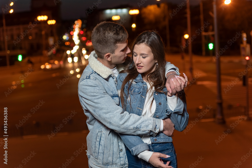 Fototapeta premium Guy gently hugs his girlfriend on evening city background. Relationship outdoors