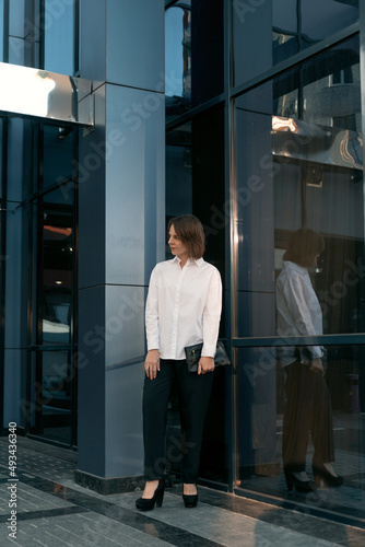 Modern business woman near office center. Formal clothes. White shirt and trousers. Full-length portrait.