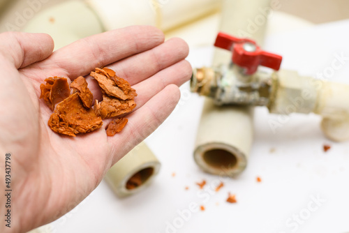 Rusty dirt and scale from polypropylene water pipes in a man's hand. Selective focus on a pile of dirt. Plumbing repair concept.