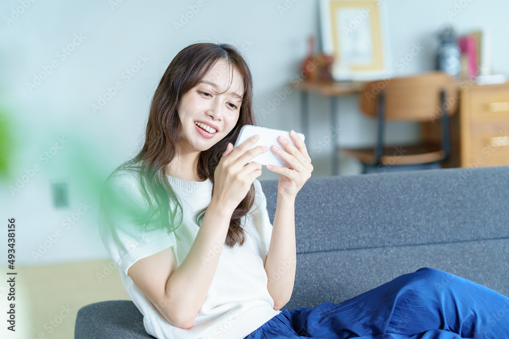 ソファに座ってスマートフォンを操作する女性 ソファに座ってスマートフォンを操作する女性
