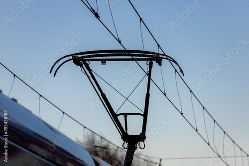 Pantograph of a tram connecting on electric line with blue sky as background, Electric railway train and power supply lines, Cables connections and metal pole overhead catenary wire. photo