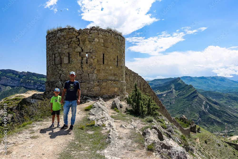 A man with a child on the background of the Gunib fortress. A protective wall. Russia, Dagestan. June 2021.