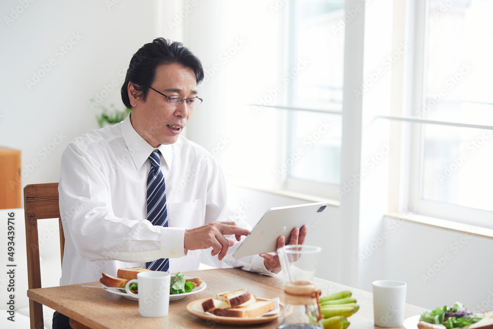 タブレット端末を見ながら朝食をとる男性 タブレット端末を見ながら朝食をとる男性