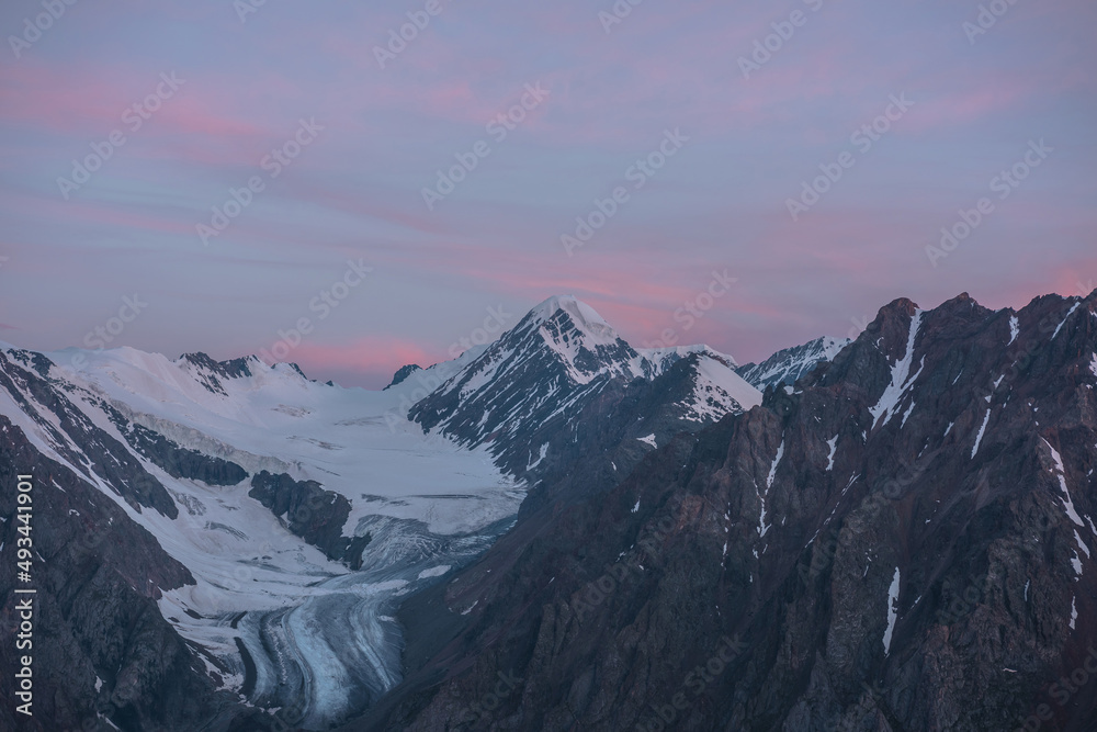 Scenic aerial view to high snow mountains in early morning in sunrise colors. Awesome scenery with pinnacle in pink cloudy sky at dawn. Morning landscape with snow mountain peak under pink clouds.