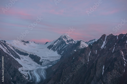 Scenic aerial view to high snow mountains in early morning in sunrise colors. Awesome scenery with pinnacle in pink cloudy sky at dawn. Morning landscape with snow mountain peak under pink clouds.