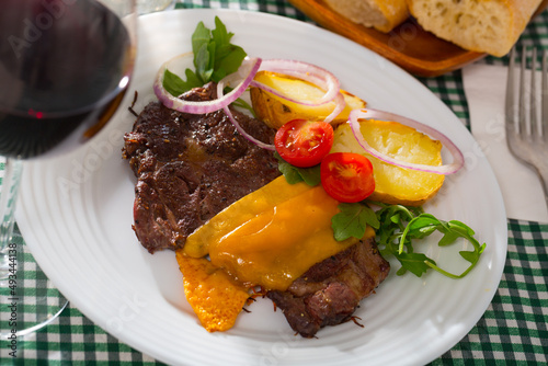 Well-done beef steak with cheese and baked potatoes at plate with greens