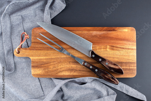 Fork and knife for meat on the wooden board with grey apron on black background photo