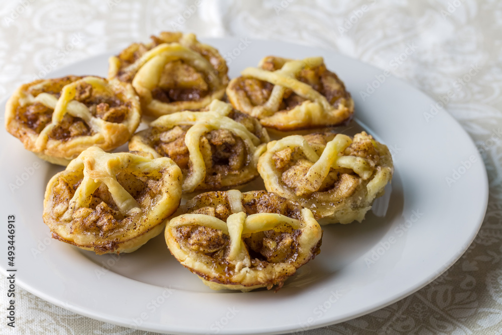 Little apple pies with cinnamon and dough decoration on a plate - apple tartlets close up with selective focus Little apple pies with cinnamon and dough decoration on a plate - apple tartlets close up with selective focus