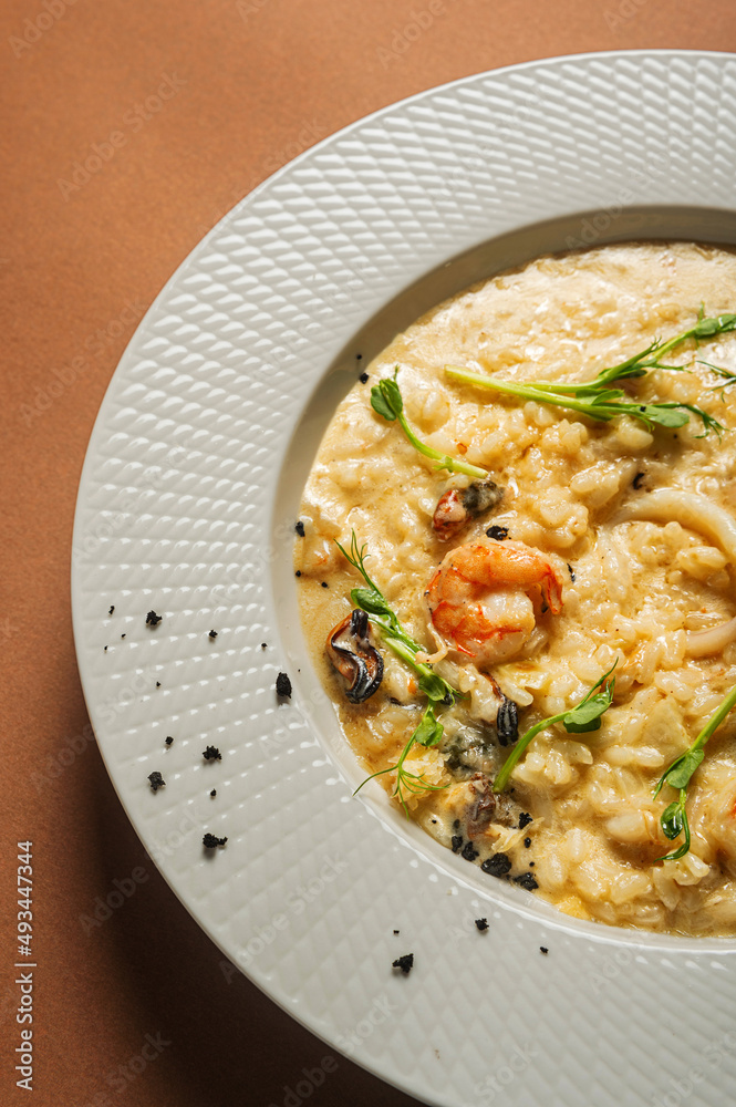 Appetizing risotto with seafood (shrimp and mussel) garnished with microgreens (pea sprouts) in a beautiful white plate.