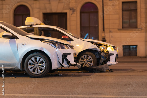Two cars on the city road after collision. Damaged white automobile on the street after the accident with damaged bumpers, side view. 