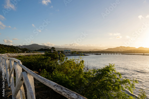 Fototapeta Naklejka Na Ścianę i Meble -  Sunset at Puerto Plata. Beautiful sky at sunset over green hill and rural white fence. Colorful and vibrant clouds. The soft light of the setting sun.