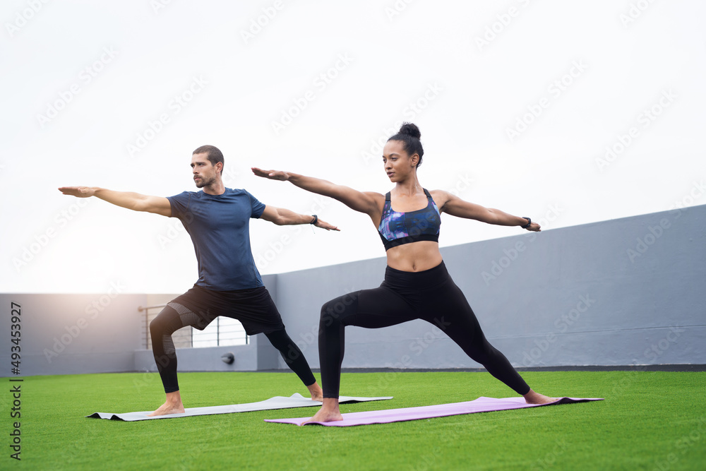 Fototapeta premium Maintaining balance and form is key. Shot of a young man and woman practising yoga together outdoors.