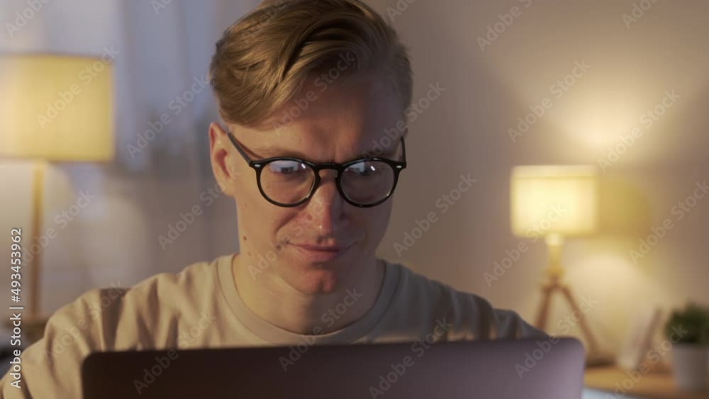 Young Caucasian Freelancer Man Working on Computer at Home at Night. Casual Concentrated Entrepreneur Developing New project While Working on Laptop Typing, Scrolling, Surfing Web, Looking at the Young Caucasian Freelancer Man Working on Computer at Home at Night. Casual Concentrated Entrepreneur Developing New project While Working on Laptop Typing, Scrolling, Surfing Web, Looking at the