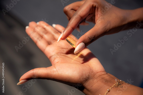 Yellow gel oil capsule of pill  Omega or vitamin D3  in the hands of African ethnicity woman close up