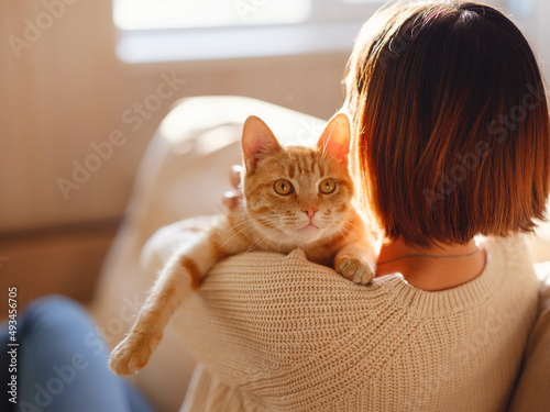 Billede på lærred Young asian woman wears warm sweater resting with tabby cat on sofa at home one autumn day