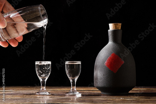 Fotografie chinese liquor is poured into a glass from a bottle on wood background