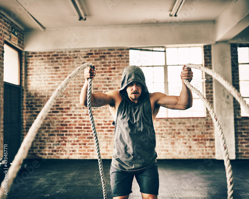 Ropes arent just for tying things. Shot of a hooded and determined young man making use of ropes to workout in the gym. photo