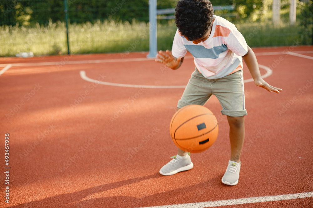 Multiracial boy standing on a basketball court and play with an orange ball