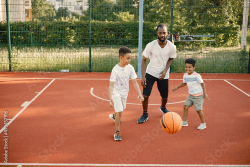 Black father with two his multiracial sons playing basketball in basketball court together © prostooleh
