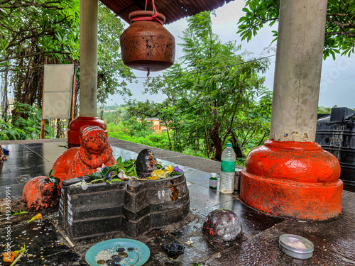 Canvas Print Stock photo of ancient shivling made up by black stone with bull statue painted by saffron color, clay made pot hanging above the shivling