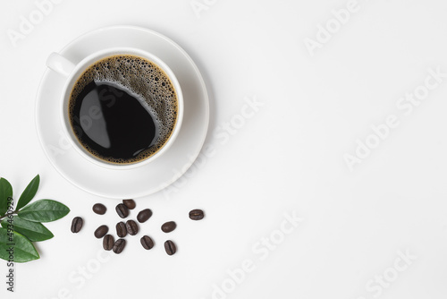Black coffee in a cup and coffee beans with green leaves isolated on a white background.