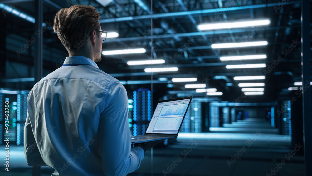 Data Center Male It Specialist Using Laptop while Working on Computer. Information Technology Professional. Server Farm Cloud Computing and Cyber Security Maintenance Concept Data Center Male It Specialist Using Laptop while Working on Computer. Information Technology Professional. Server Farm Cloud Computing and Cyber Security Maintenance Concept