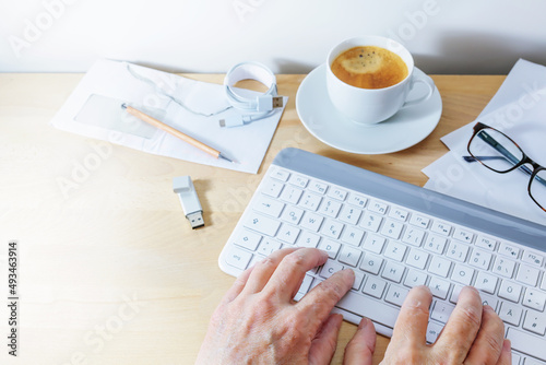 Hands using a computer keyboard on an office desk with coffee, usb stick and papers, business at home concept, copy space, selected focus