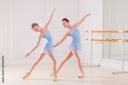 Young ballerinas having rehearsal at studio. Row of happy young ballerinas practicing at ballet barre, focus on first girl.