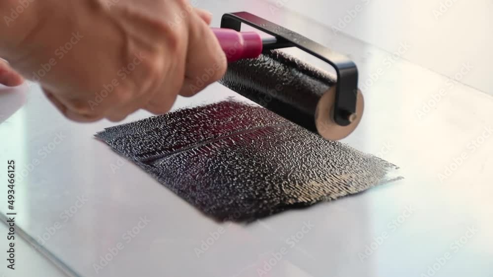 Woman using brayer roller with black ink for lino print