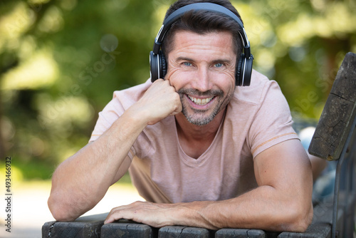 young man with headphones lying on a park bench outdoors photo