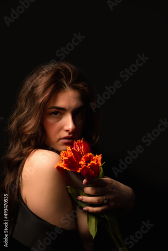 Studio portrait of a young woman in sunglasses, on a black background, with a bouquet of red tulips in her hands. International Women's Day. Valentine's Day.