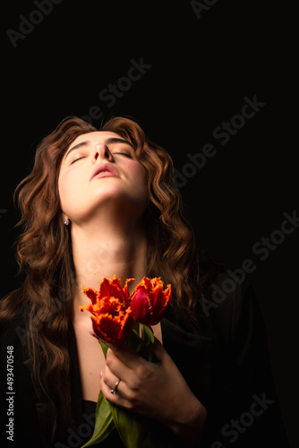 Studio portrait of a young woman in sunglasses, on a black background, with a bouquet of red tulips in her hands. International Women's Day. Valentine's Day.