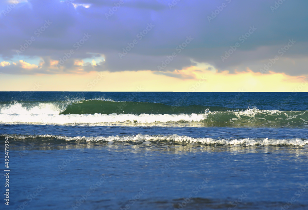 Waves in sea during a storm on sunset. Waves against backdrop of a stormy sky in sea. Waves at sea on dramatic sunset. Wave from the ocean goes on land to beach. Ocean during storm and wind. .