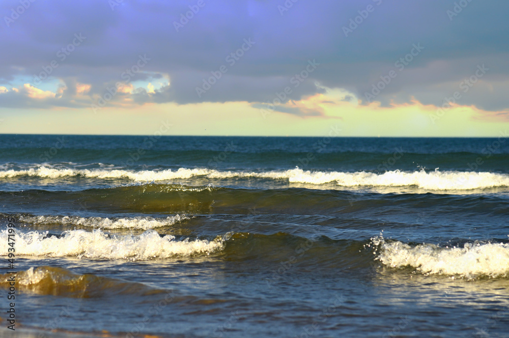 Waves in sea during a storm on sunset. Waves against backdrop of a stormy sky in sea. Waves at sea on dramatic sunset. Wave from the ocean goes on land to beach. Ocean during storm and wind. .