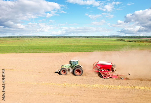 Tractor sowing seed on plowed field, drone view. Farming and seeding machinery for plowed field. Seed sowing and land cultivating. Tractor at arable. Tractor with disk harrow on plowing field. 