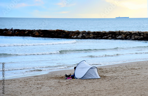 Camping in tent on beach at sea. Camping trip to beach. Man refugee in tent at coastline. Homeless man near sea. The concept of a social problem of stray, houseless, waif and unhoused people.. photo