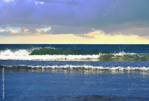Waves in sea during a storm on sunset. Waves against backdrop of a stormy sky in sea. Waves at sea on dramatic sunset. Wave from the ocean goes on land to beach. Ocean during storm and wind. .