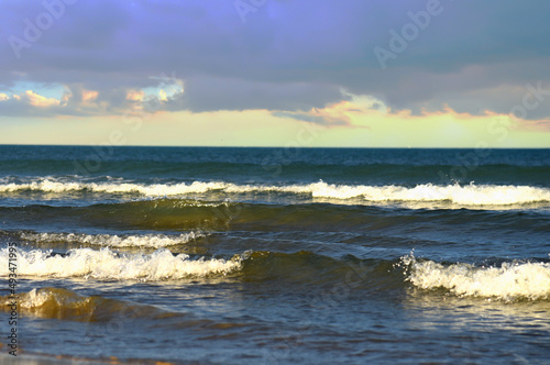 Waves in sea during a storm on sunset. Waves against backdrop of a stormy sky in sea. Waves at sea on dramatic sunset. Wave from the ocean goes on land to beach. Ocean during storm and wind. .