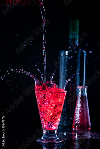 campari and vodka with splashes on dark black background and bottles behind and liquid spilled on the glass photo