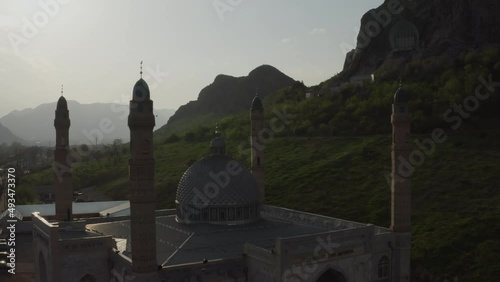 A beautiful Muslim mosque in rays of sunset sunlight against background of rocky mountains and sky. Flying a quadrocopter around a mosque in an urban environment in golden sunlight. Kyrgyzstan osh photo
