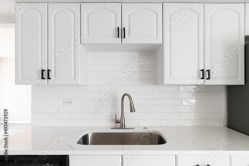 A kitchen with white cabinets, subway tiles, and marble countertop.