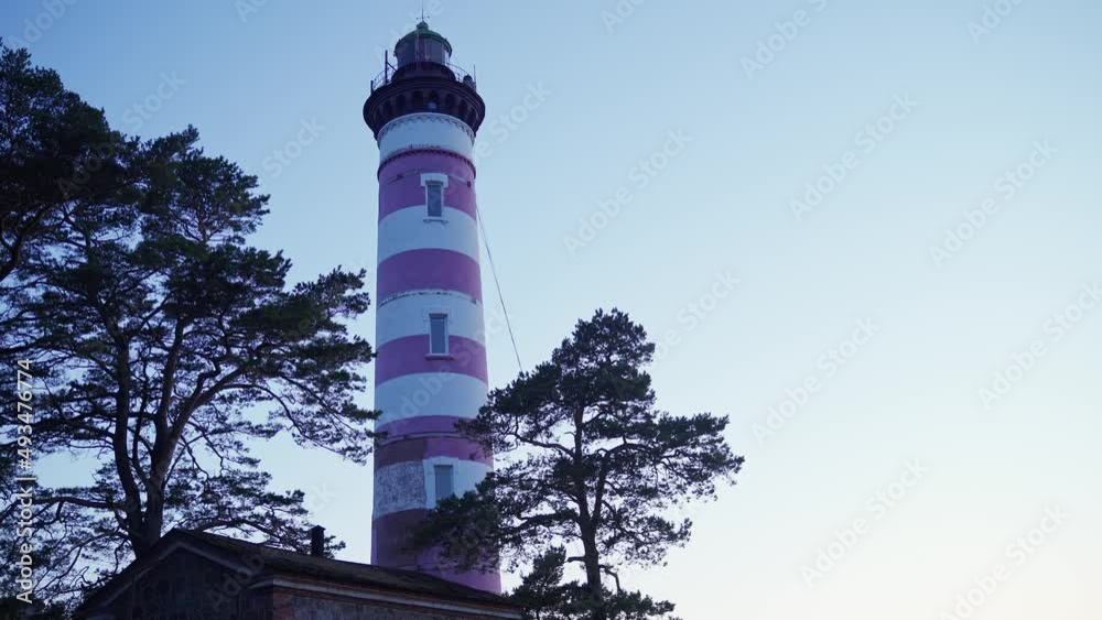 lighthouse at dusk. red and white lighthouse between two trees against the darkening sky lighthouse at dusk. red and white lighthouse between two trees against the darkening sky