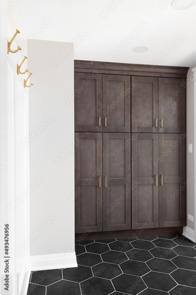 An entryway mudroom with wood cabinets, hold coat hooks, and a black hexagon tiled floor. There's a view to a deck outside. An entryway mudroom with wood cabinets, hold coat hooks, and a black hexagon tiled floor. There's a view to a deck outside.
