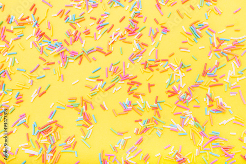 Colorful festive sugar sprinkles on yellow background. Flat lay style. Top view. Place for design. Easter background.