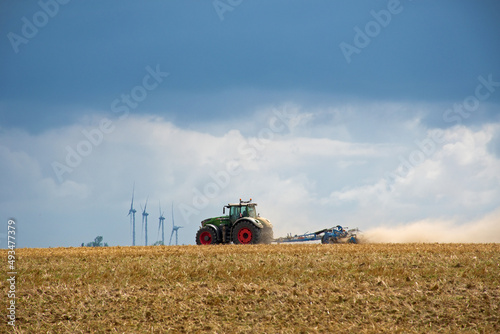 Ackerbau in der Picardie, Frankreich. Traktor auf dem Feld mit Windrädern im Hintergrund und dicken Wolken