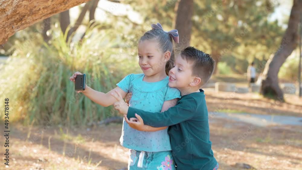 Niños felices tomándose fotos fotografías selfies retrato con el celular jugando y disfrutando en el parque abrazados al aire libre en tronco café de un árbol