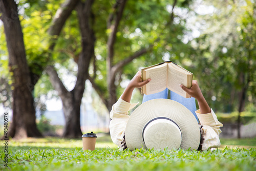 Woman reading book in grass under tree with cup of coffee. Relax in summer time holiday laying on the grass field comfortable feeling.