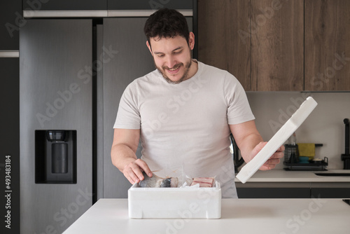 Young latin man opening his weekly delivery of fish in an EPS isothermal box, in the kitchen. photo