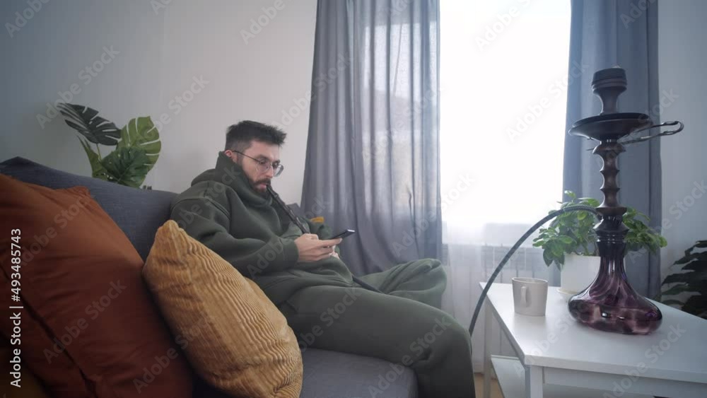 Rest and relaxation concept. Man smokes a hookah in room of home interior Rest and relaxation concept. Man smokes a hookah in room of home interior